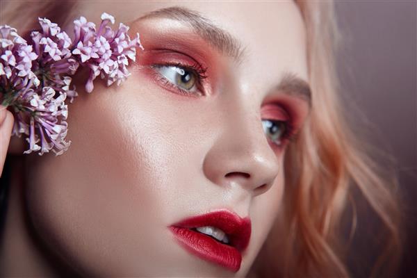 پرتره زنی بلوند با گلبرگ های گل روی صورتش آرایش قرمز روشن و رژ لب آبرسانی پوست مراقبت از صورت اثر ضد پیری لوازم آرایشی
