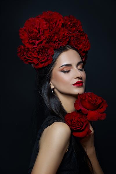 پرتره زیبایی زن سبزه با تاجی از گل های رز روی سرش آرایش قرمز روشن و رژ لب گل های رز در دستان یک زن