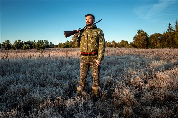 مرد شکارچی در استتار با تفنگ در حین شکار در جستجوی پرندگان وحشی