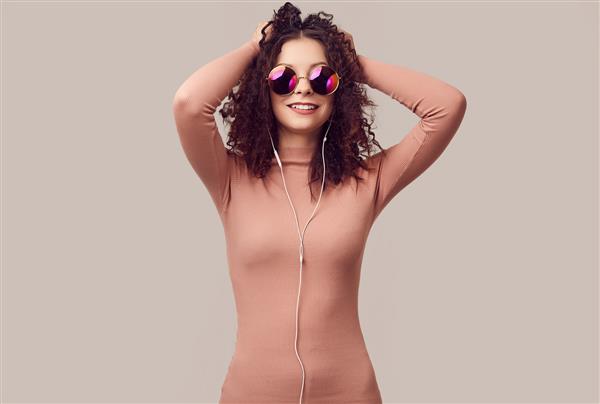 دختر خوشگل و زیبا با موهای مجعد در حال گوش دادن به موسیقی با هدفون