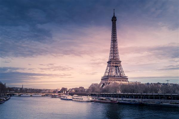 عکس وسیع زیبا از برج ایفل در پاریس که توسط آب با کشتی ها در زیر آسمان رنگارنگ احاطه شده است