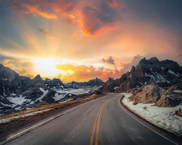 جاده ای که توسط کوه های صخره ای در هنگام غروب زیبای خورشید در عصر احاطه شده است