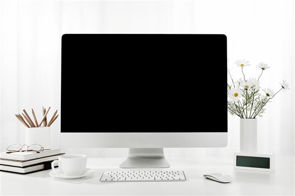 نمای نزدیک از یک کامپیوتر یک فنجان قهوه یک گلدان گل و موارد دیگر روی یک میز سفید در داخل خانه