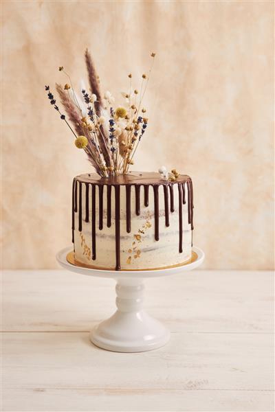 عکس عمودی از کیک بوهو خوشمزه با قطره شکلات و گل در بالا با تزئینات طلایی