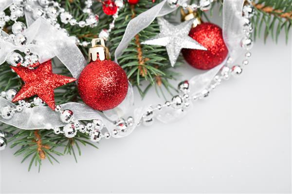 دکور کریسمس در زمینه سفید شاخه درخت کریسمس ستاره های قرمز توپ شیشه ای براق گلدسته نقره ای و روبان