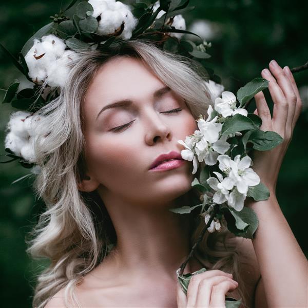 دختر مدل بهاره با شکوفه های سیب سفید زن زیبا با پوست سالم و تاج گل در فضای باز