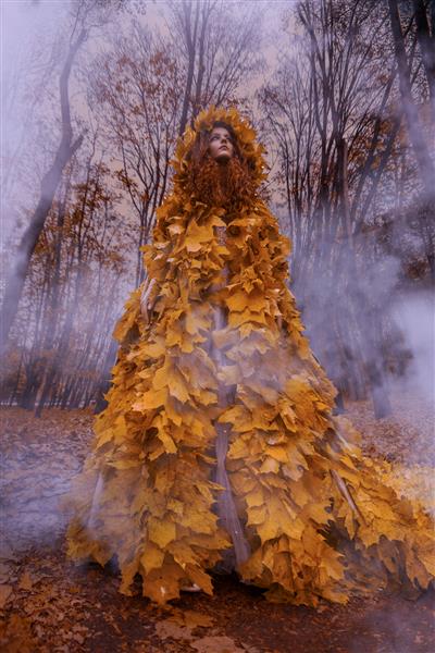 دختر مو قرمز زیبا به عنوان یک پاییز در شنل برگ در جنگل