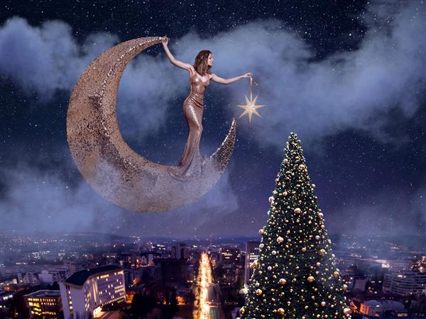زن زیبا روی ماه می ایستد و ستاره ای را به درخت کریسمس آویزان می کند