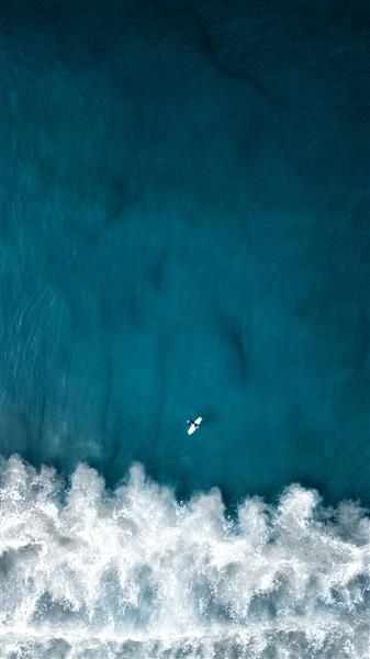 عکس عمودی بالای سر هوایی از امواج زیبای اقیانوس با هواپیمایی که در بالا پرواز می کند