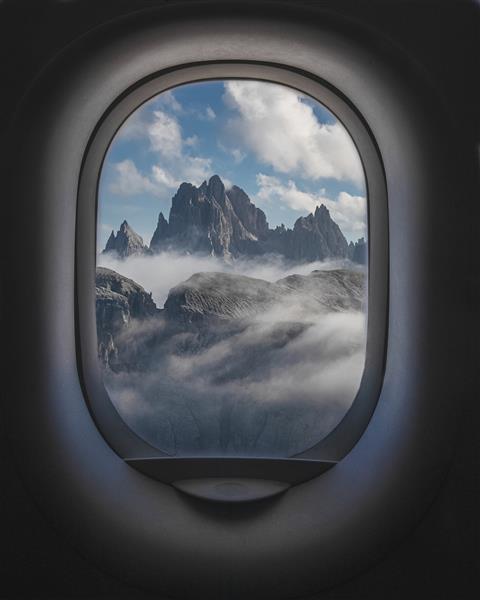 تصویری زیبا از کوه و آسمان ابری از داخل پنجره هواپیما