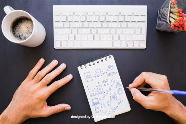 میز اداری و طراحی دست با خودکار روی دفترچه یادداشت