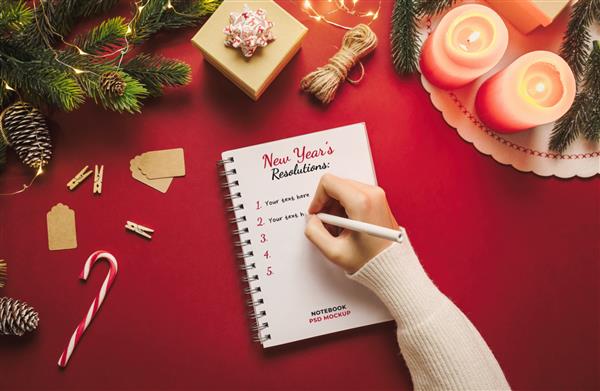 دست نوشته در مدل نوت بوک با وضوح سال جدید با چیزهای کریسمس در پس زمینه قرمز