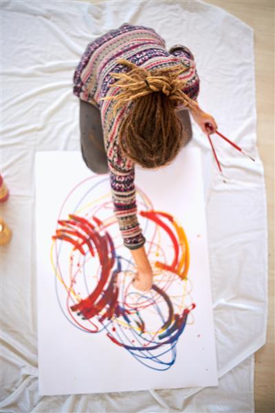 نمایی هوایی از دختر هنرمندی که در استودیو نشسته و در آتلیه اش نقاشی می کشد