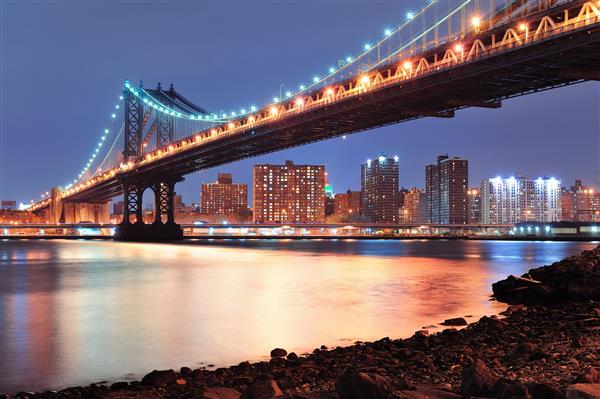 نمای نزدیک از پل منهتن شهر نیویورک با خط افق مرکز شهر بر فراز رودخانه شرقی