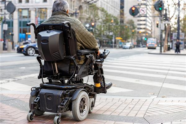 یک معلول سالخورده روی ویلچر برقی در خیابان شهر مقابل گذرگاه عابر پیاده مفهوم فناوری مدرن برای افراد دارای معلولیت