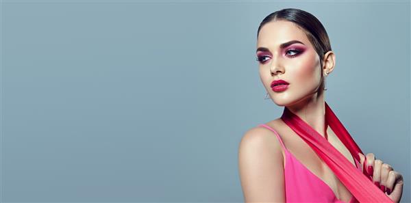 پرتره یک دختر جوان زیبا با آرایش صورتی روشن و با روبان های صورتی در دستانش