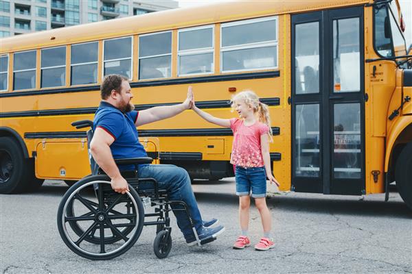 تشویق و حمایت اعضای خانواده پدر معلول قفقازی روی ویلچر با دخترش در اتوبوس زرد مدرسه بازگشت به مدرسه ژست پنج بالا بین پدر و بچه