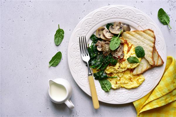 صبحانه سالم املت با اسفناج قارچ و کروتون در یک بشقاب سفید روی تخته سنگ روشن سنگ یا زمینه بتونی نمای بالا با فضای کپی