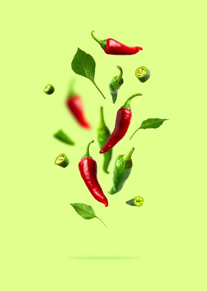 فلفل چیلی سبز و قرمز در حال پرواز برگ های جدا شده در زمینه سبز ادویه برای غذا فلفل تند تازه ادویه های تند برای پخت و پز فلفل قرمز غذا مفهوم خلاقانه غذا سبزیجات
