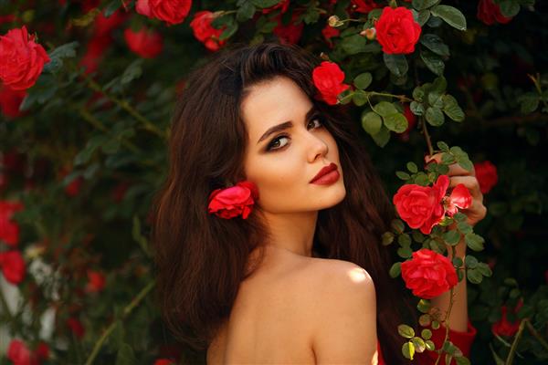 پرتره بیرون از خانه از زن زیبای طبیعی با گل رز قرمز زن شهوانی با گل های رز در مو سبزه زیبا با آرایش در پارک شکوفه غروب آفتاب اشتیاق و بیان سبک فلامنکو اسپانیایی