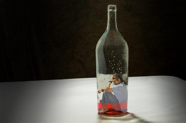 اعتیاد به الکل توسط مردی که در داخل یک بطری مشروب به دام افتاده است به تصویر کشیده شده است