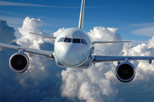 هواپیمای تجاری در حال پرواز بر فراز پس زمینه ای پوشیده از ابر