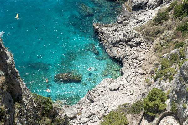 کاپری ایتالیا 26 ژوئن 2015 نمای بالای خط ساحلی صخره ای جزیره با چند شناگر در دریای زیبای زمرد در کاپری
