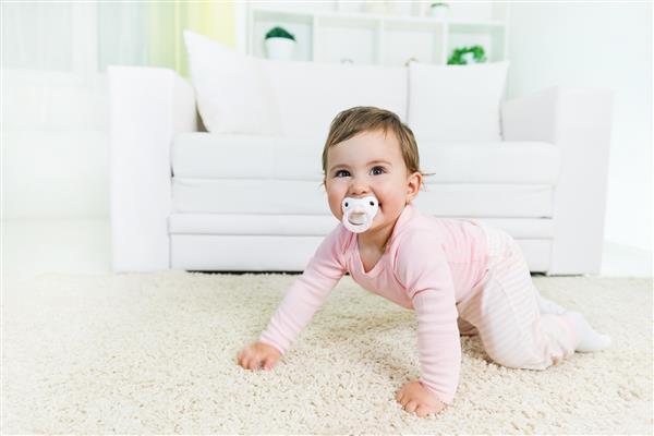 دختر بچه شادی که با پستانک در دهانش در کف اتاق نشیمن می خزد و به دوربین نگاه می کند فضای کپی