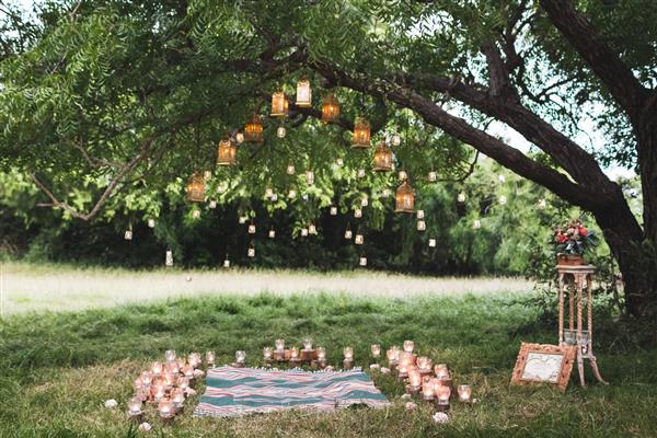 مراسم عروسی عصر با یک قالیچه و تعداد زیادی لامپ و شمع قدیمی روی درخت بزرگ سبک روستیک