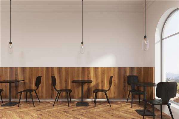 صندلی‌های مشکی مدرن در نزدیکی میزهای چوبی مربعی در یک کافی‌شاپ یا یک رستوران با کف چوبی و دیوارهای سفید ایستاده‌اند رندر سه بعدی