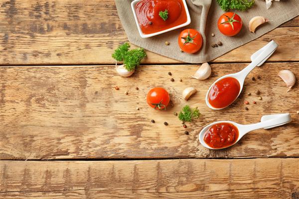 قاشق های سرامیکی با سس گوجه فرنگی و ادویه جات روی میز چوبی