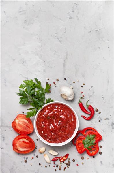 سس گوجه فرنگی در یک کاسه سفید گوجه فرنگی تازه و جعفری در زمینه بتونی خاکستری نمای از بالا