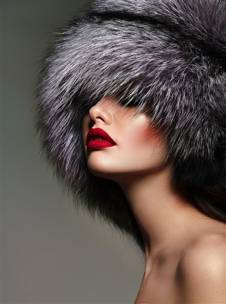 پرتره یک دختر جوان زیبا با لب های قرمز در کلاه خز کرکی ساخته شده از روباه قطبی