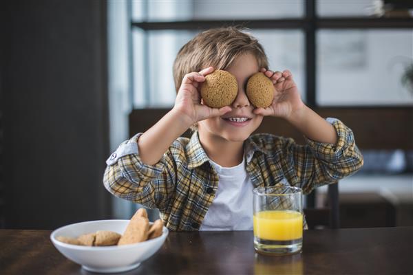 نمای مبهم پسر کوچکی که هنگام صرف صبحانه در خانه چشمانش را با کلوچه در دست می پوشاند