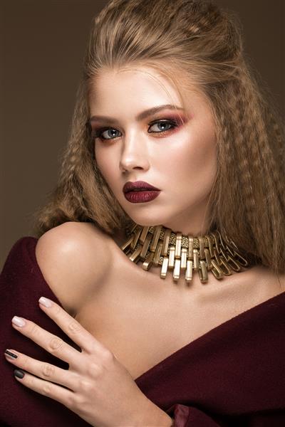 مدل بلوند زیبا با فر آرایش روشن جواهرات طلا و لب های قرمز زیبایی صورت پرتره ای که در استودیو روی پس زمینه قهوه ای گرفته شده است