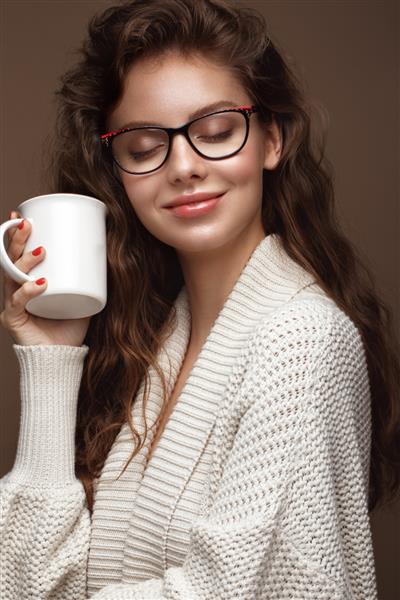 دختر زیبا در یک ژاکت دنج با یک فنجان چای عینک برای بینایی و لب های جذاب صورت زیبایی عکس گرفته شده در استودیو