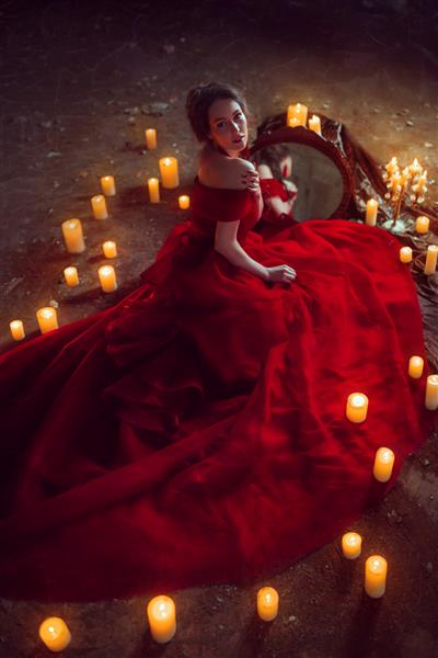 خانم زیبا با لباس مجلسی قرمز با شمع نشسته است