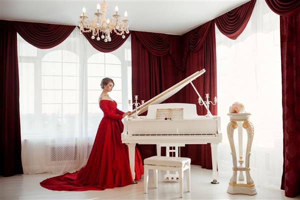 یک زن زیبای جوان با لباس شب قرمز پشت پیانوی بزرگ نشسته است