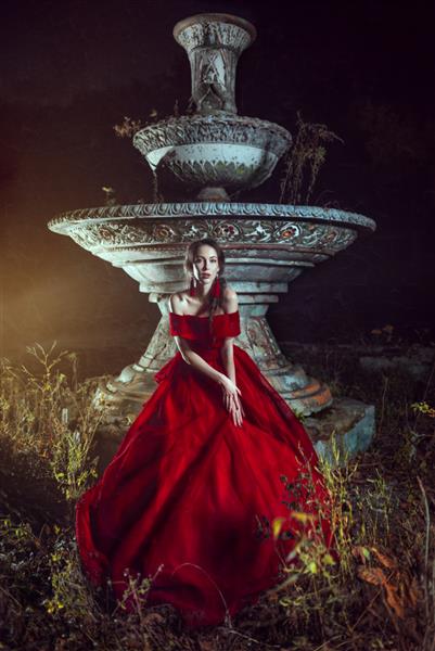 خانم زیبا با لباس مجلسی قرمز که نزدیک چشمه می ماند