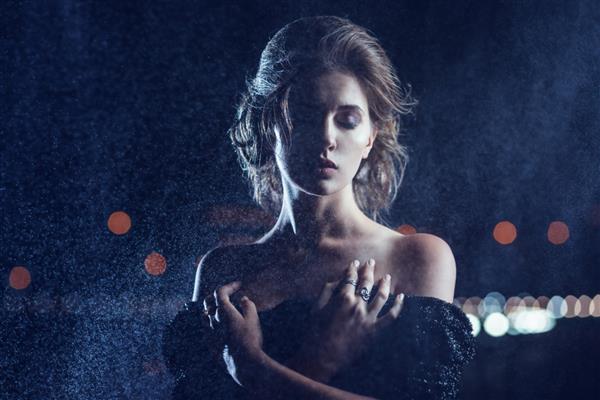 زن زیبا با لباس مشکی که روی پس‌زمینه چراغ‌های شهر ژست گرفته است