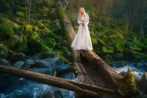 زن جوان زیبا با لباس سفید در وسط جنگل قدم می زند