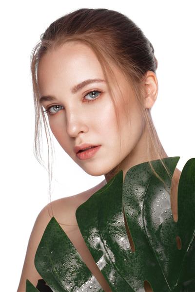 دختر زیبای شاداب با آرایش طبیعی پوستی عالی و برگ های سبز عکس چهره زیبایی که در استودیو گرفته شده است
