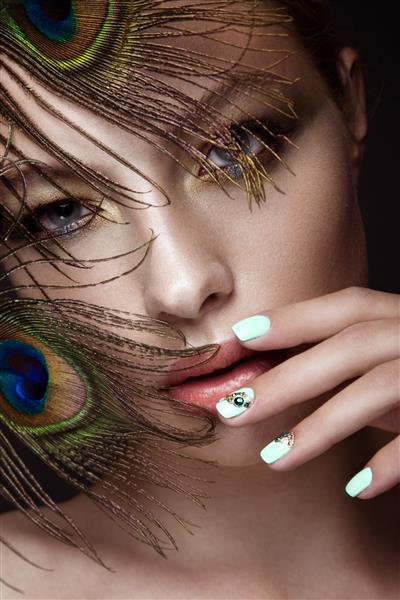 دختر زیبا با طرح مانیکور آرایش روشن و پر طاووس روی ناخن های هنری صورتش