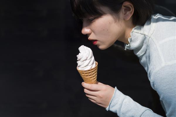نمای جانبی زن جوانی که قیفی بستنی در دست دارد