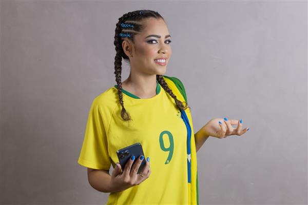 زن طرفدار برزیلی در حال تشویق برزیل در جام جهانی 2022 در تماس ویدیویی در حال صحبت با دوستان از راه دور تلفن همراه با فناوری ارتباطی تلفن همراه