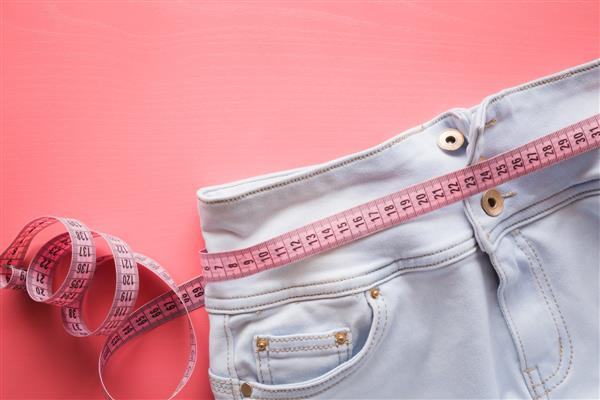 نوار را با شلوار جین آبی روشن روی زمینه صورتی پاستلی اندازه بگیرید رژیم غذایی زنان الگوی سبک زندگی سالم لاغری بدن کاهش وزن یا پیشنهاد خیاطی یا ایده های دیگر جای خالی متن