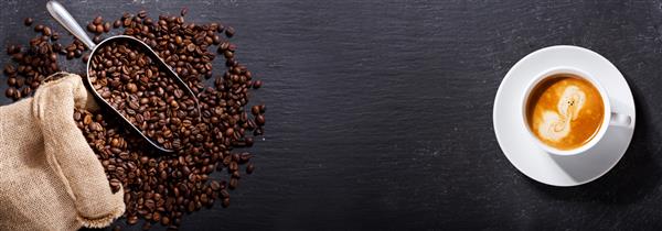 فنجان قهوه و دانه های قهوه در گونی در پس زمینه تیره نمای بالا