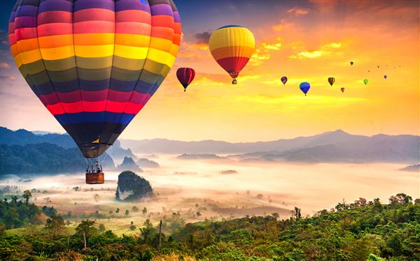 نمایی هوایی از بالون‌های رنگارنگ هوای گرم که با مه در پارک ملی فو لانگکا در زمان طلوع آفتاب استان فایائو در تایلند پرواز می‌کنند