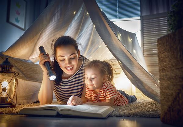 زمان خواب خانواده مادر و دختر در چادر مشغول خواندن کتاب هستند مادر جوان زیبا و دختر دوست داشتنی در حال تفریح در اتاق کودک