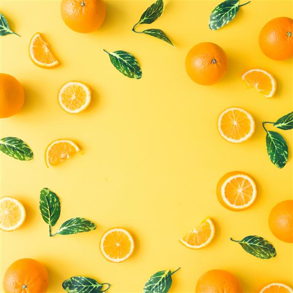 الگوی تابستانی خلاقانه ساخته شده از پرتقال و برگ های سبز در زمینه زرد پاستلی مفهوم مینیمال میوه تخت دراز کشید
